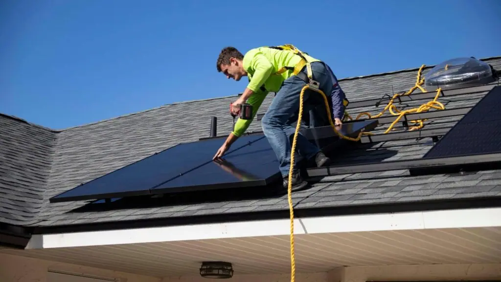 A technician in hi-vis on a roof cleaning solar panels with a water-fed hose