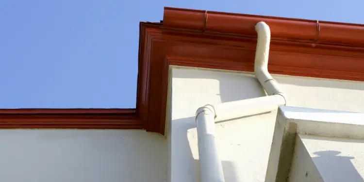 Red roofline guttering and a white downpipe on a rendered building against a blue sky